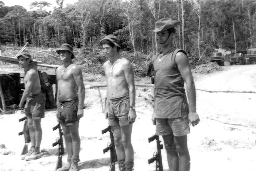 Four soldiers coming to attention on  sand in front of the jungle.