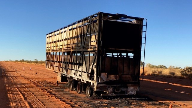 a burnt-out road train trailer in the middle of the road.