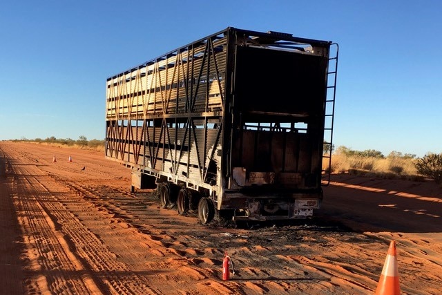 The burnt-out remains of a livestock trailer sitting in the middle of a red road.