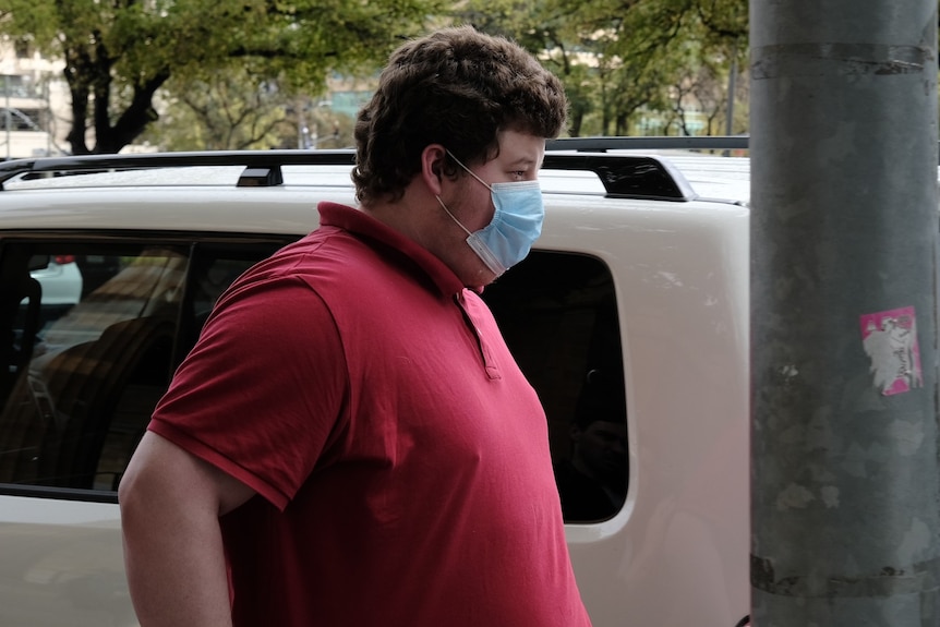 A man wearing a red polo shirt and a face mask