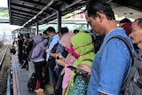 Couple of people look into their mobile phones while waiting for a train.