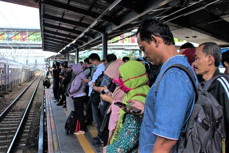 Couple of people look into their mobile phones while waiting for a train.