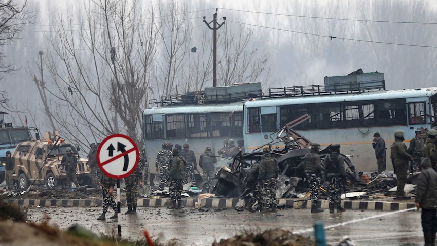 Indian paramilitary soldiers stand by the wreckage of a bus after an explosion.