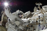 An astronaut holding onto the outside of a spacecraft with one arm raised