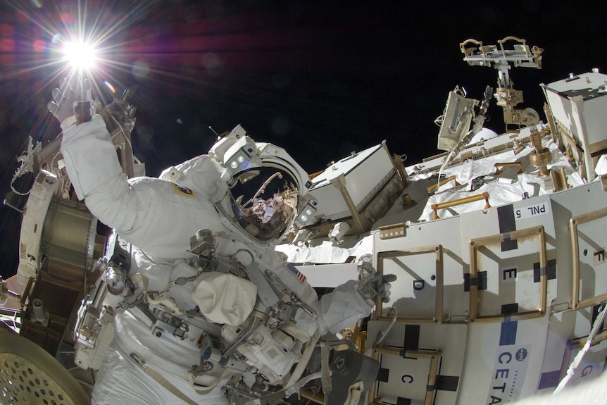 An astronaut holding onto the outside of a spacecraft with one arm raised
