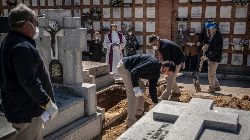 A priest and relatives pray as a victim of the COVID-19 is buried by undertakers at the Almudena cemetary in Madrid.