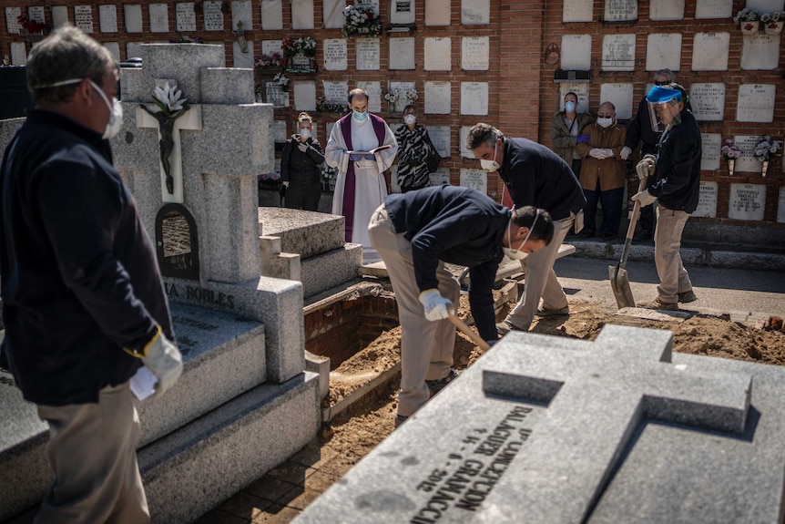 A priest and relatives pray as a victim of the COVID-19 is buried by undertakers at the Almudena cemetary in Madrid.