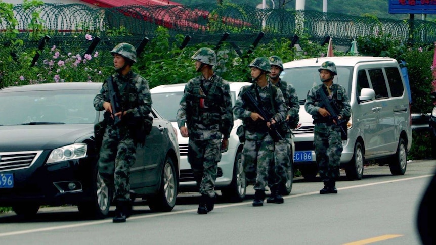 A group og Chinese troops walk down a street next to barbed wire fencing.