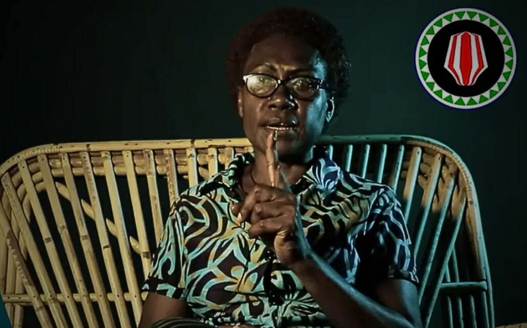 Headshot of woman sitting on chair, dark background. 