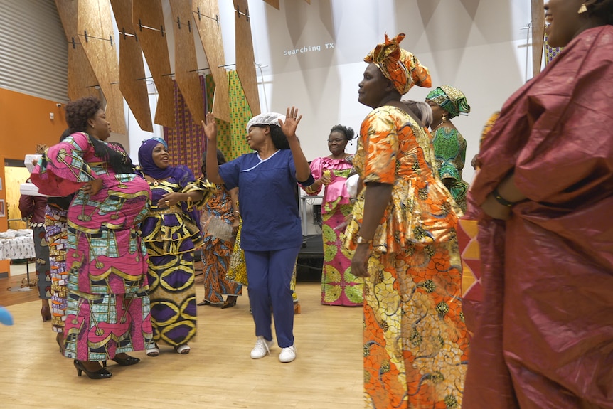 Congolese women in traditional dresses dance in a hall together.
