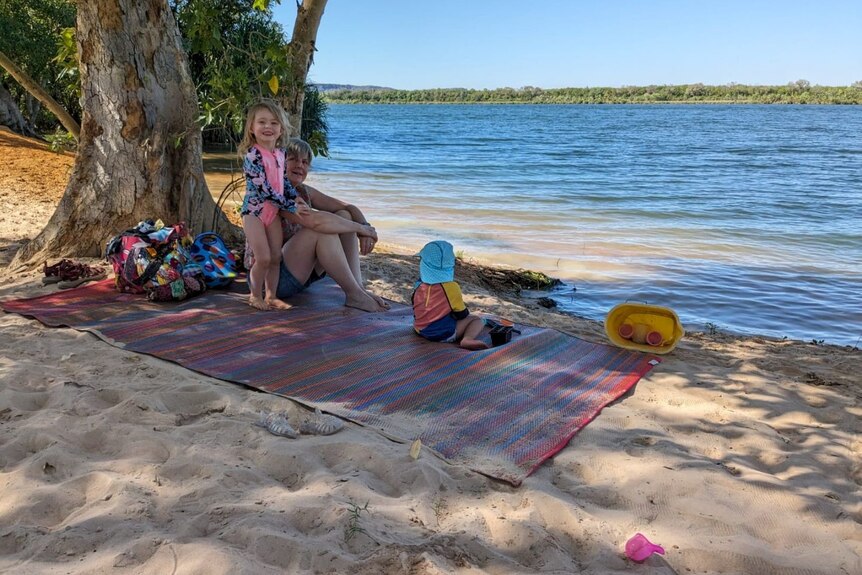 two children on a mat on sand next to a wide river