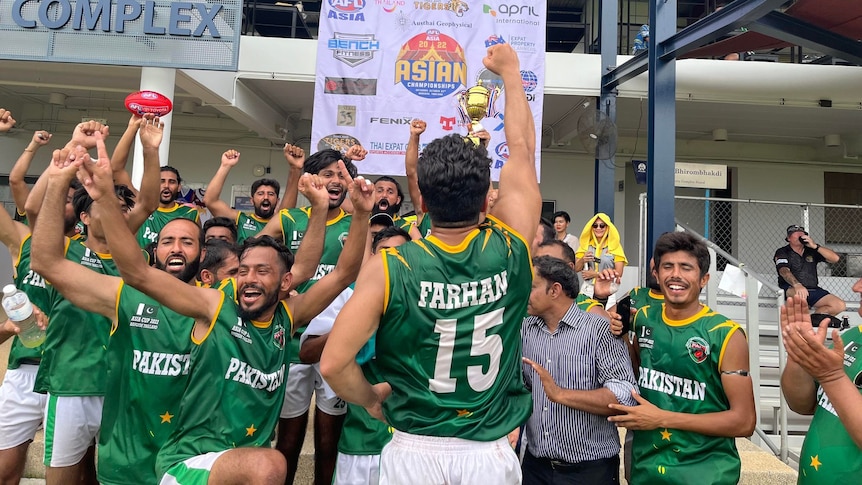 A group of men in green singlets pump their fists in the air and raise a trophy