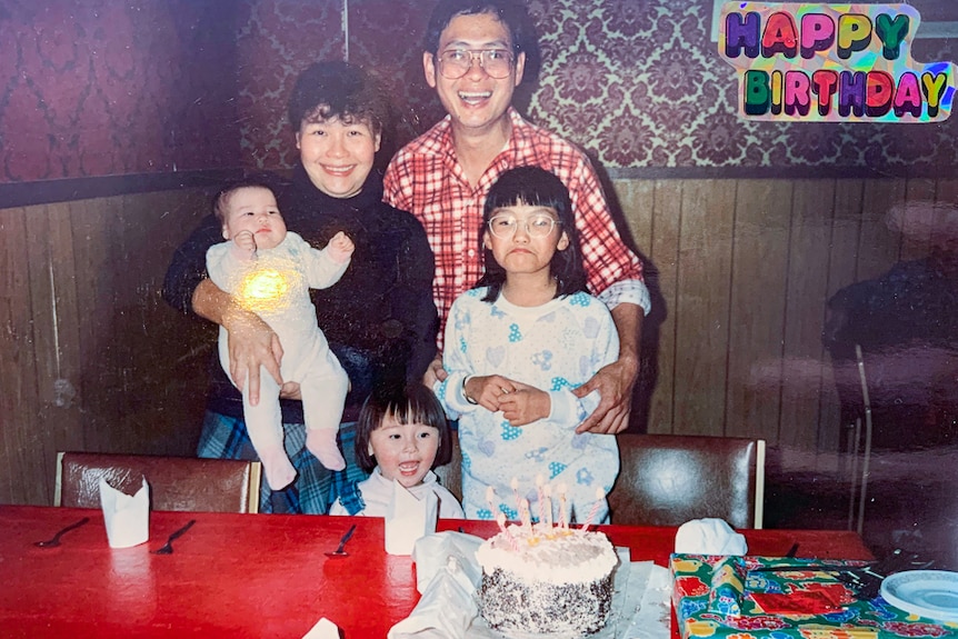 A Chinese family standing with a birthday cake inside their restaurant's dining room.