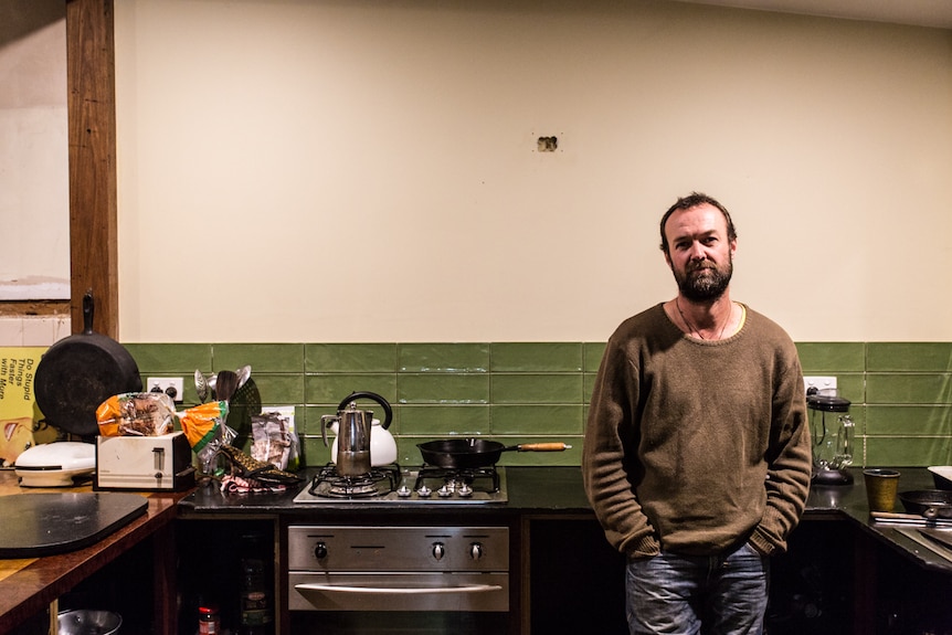 Taron at home in his kitchen leaning on a bench.