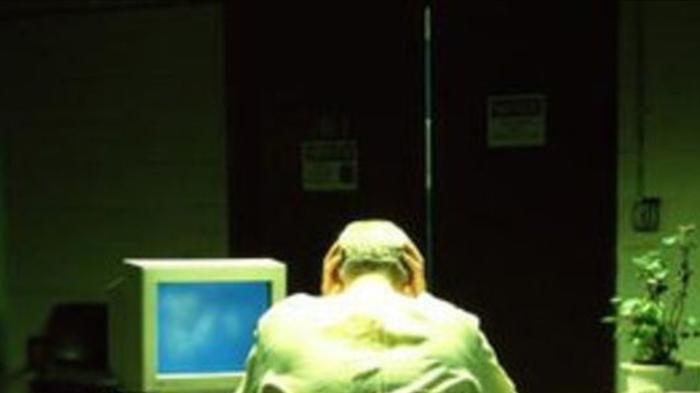 A man sits at a desk with his head in his hands