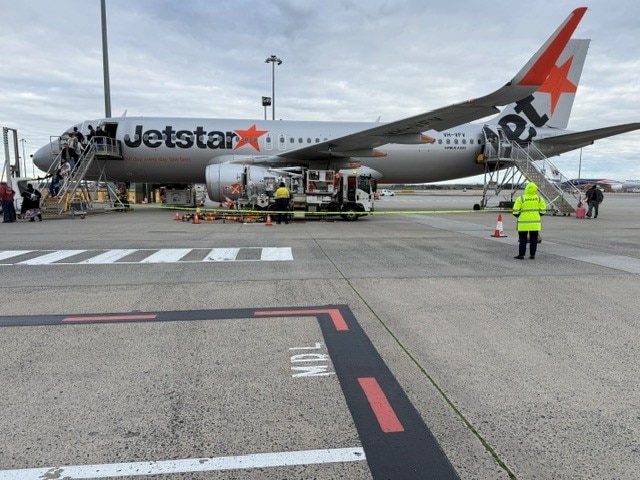 A Jetstar ground crew taking a photo of a plane on the tarmac with people disembarking.