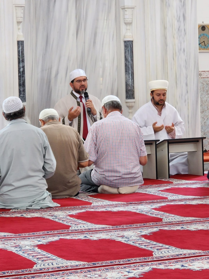 A man leading prayer with people kneeling before him. 