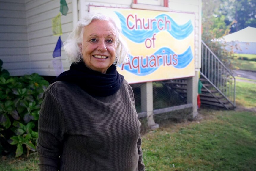 A woman with white hair outside a building that has a sign saying 'Church of Aquarius'