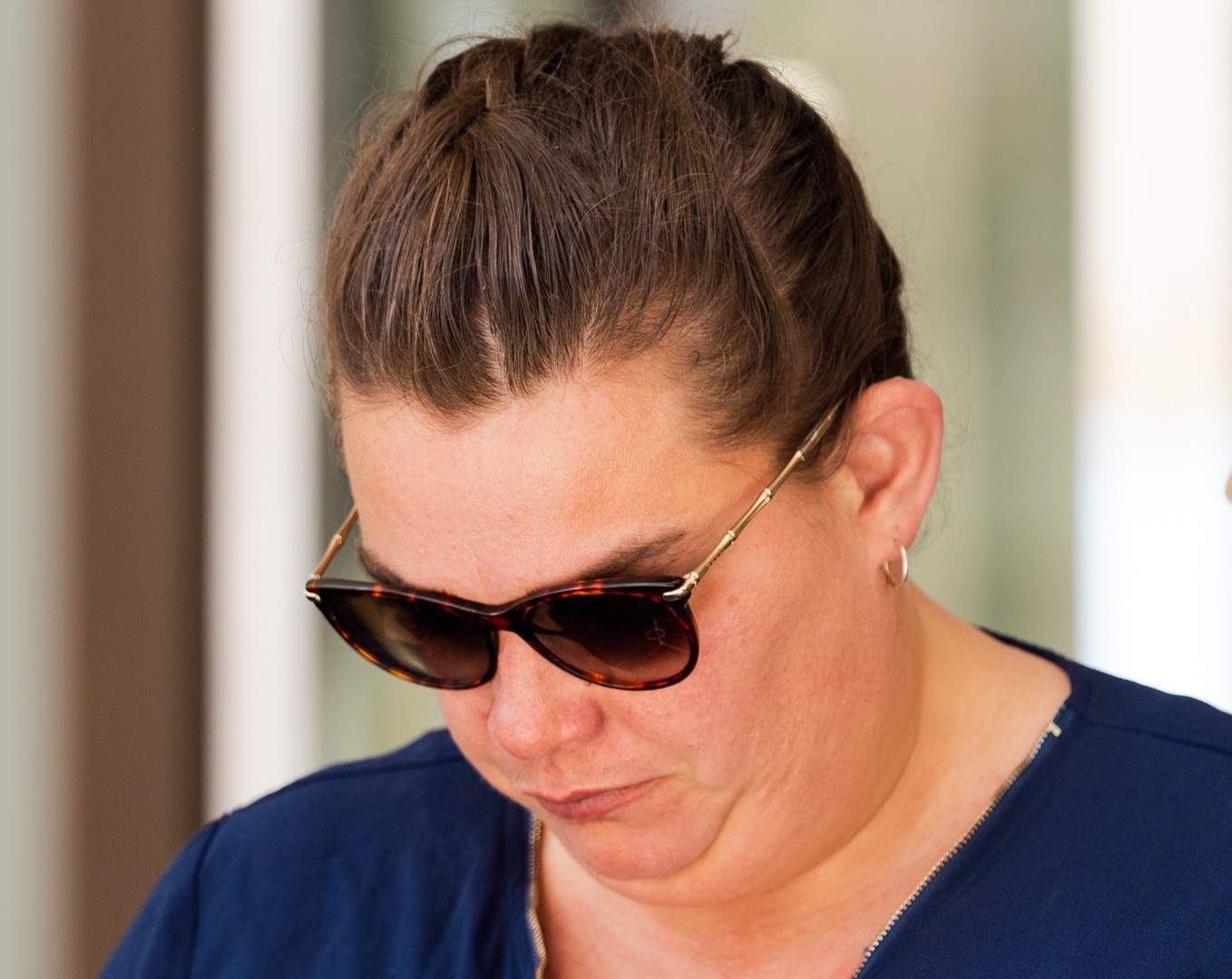 A woman with sunglasses looks down as she walks out of court.