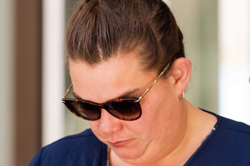 A woman with sunglasses looks down as she walks out of court.