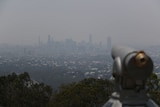 An out of focus telescope with a smokey city skylinein the background