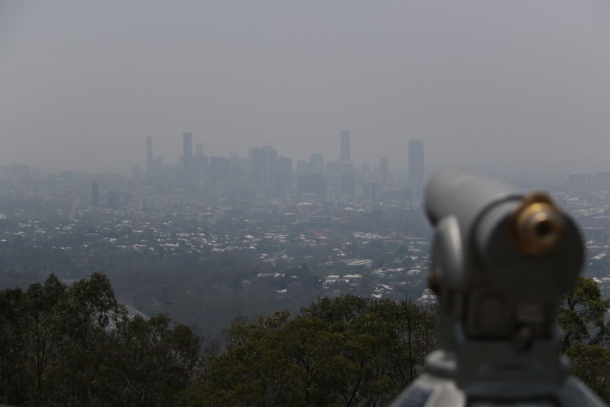 An out of focus telescope with a smokey city skylinein the background