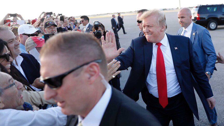 US President Donald Trump bites his lip as he high-fives supporters on the runway. He is surrounded by Secret Service agents.