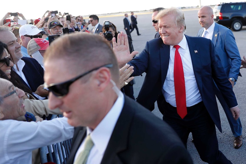 US President Donald Trump bites his lip as he high-fives supporters on the runway. He is surrounded by Secret Service agents.