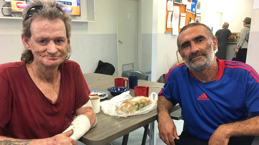 Mark King and Rob Gatani sit at a table, with food and cups behind them.