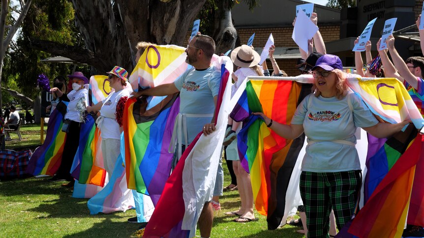 People with rainbow flags dance outside a library.