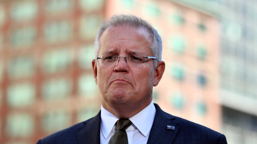 Scott Morrison stands in front of a city skyline. He is frowning.
