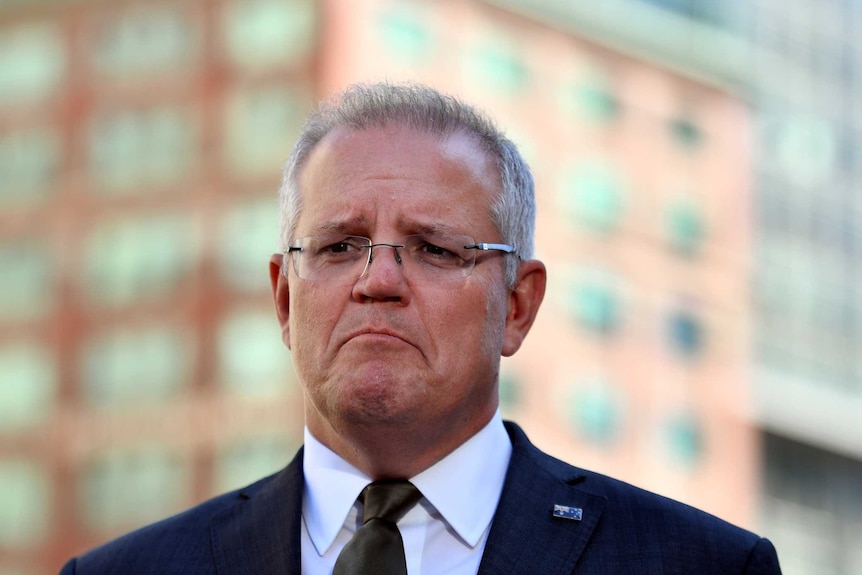 Scott Morrison stands in front of a city skyline. He is frowning.
