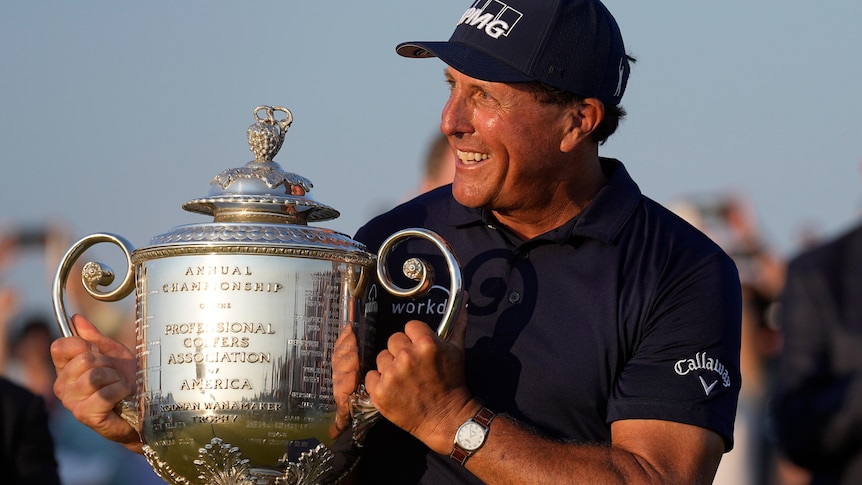 Phil Mickelson smiles while he holds up a large and shiny trophy at the PGA Championship
