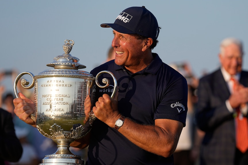 Phil Mickelson smiles while he holds up a large and shiny trophy at the PGA Championship