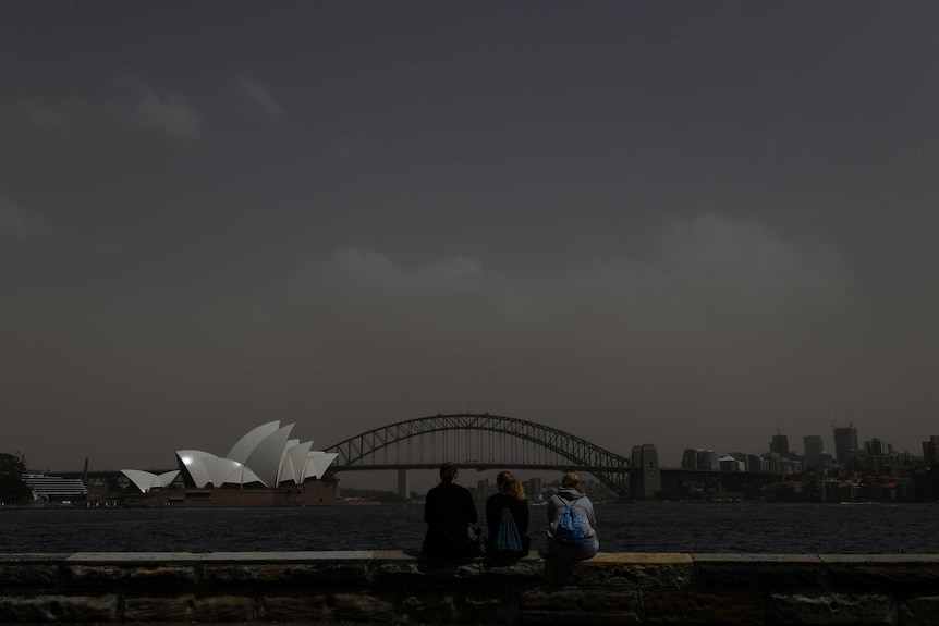 Determined tourists pose for photographs in eerily-dark Sydney Harbour as city is covered in shroud of dust in the morning.