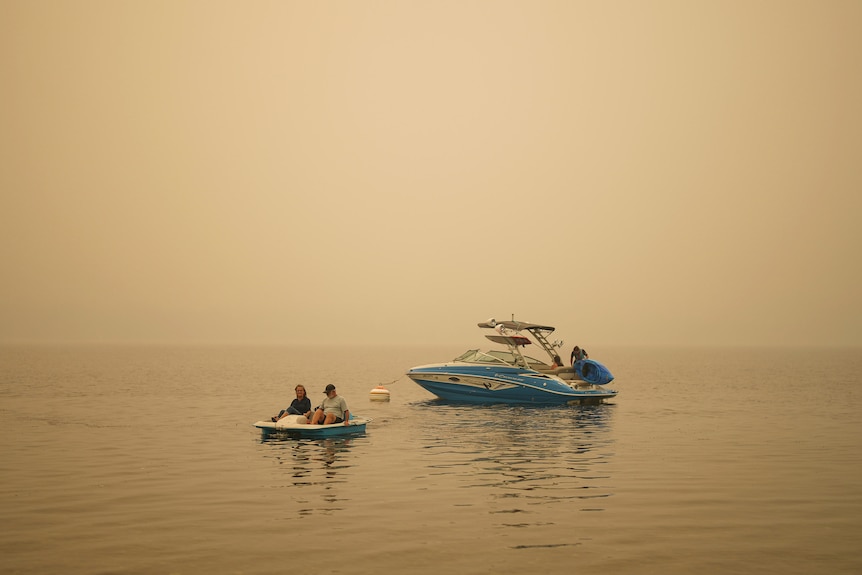 A middle-aged couple on a paddleboat in a lake, shrouded in an orange haze of bushfire smoke.