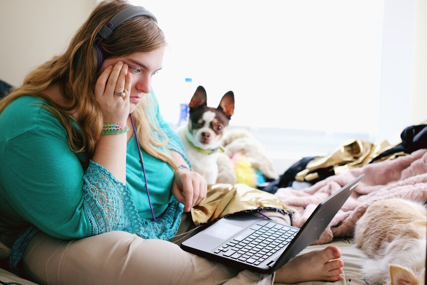 Worried looking woman in long teal top looking at computer laptop next to small dog