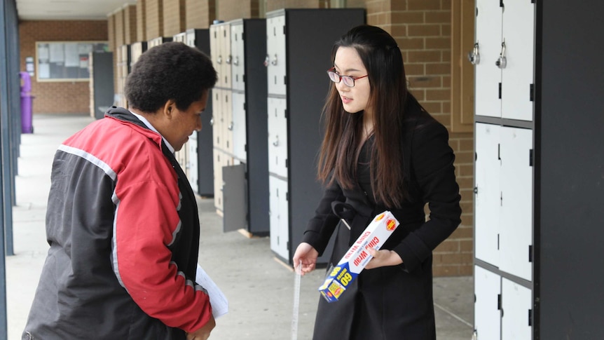 Rowenna Kalimba (left) and Lori Lu (right) talk in front of a bank of lockers at a high school.