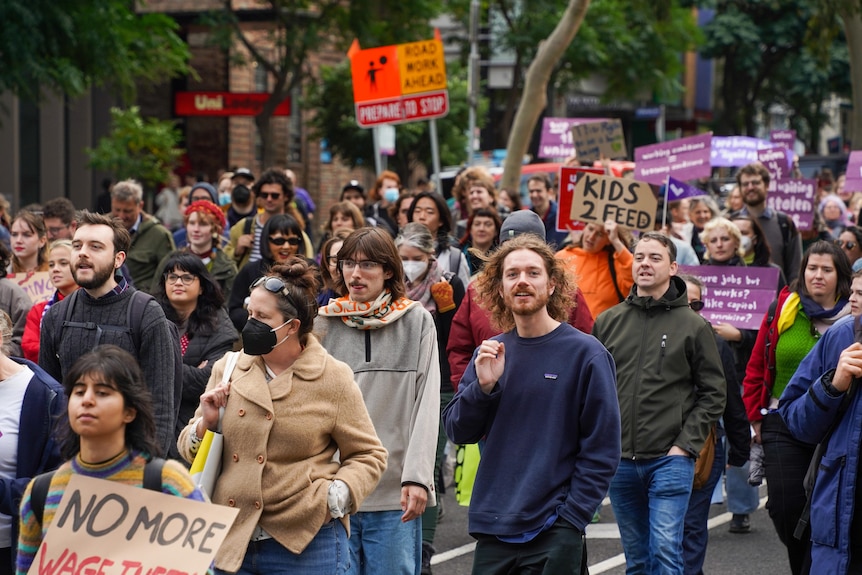 A crowd of protesters wearing warm clothing march down a street in Melbourne holding protest signs.