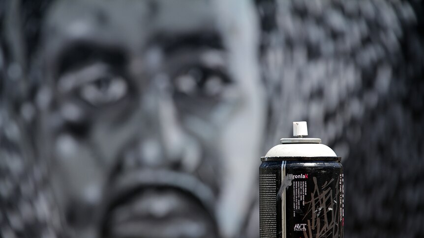 Close up shot of a spray can. Mural can be seen blurred out in the distance.
