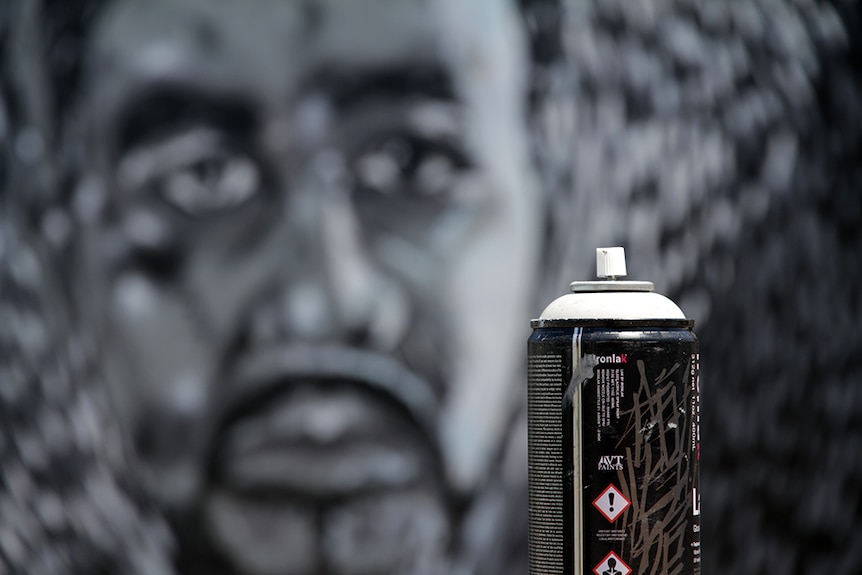 Close up shot of a spray can. Mural can be seen blurred out in the distance.