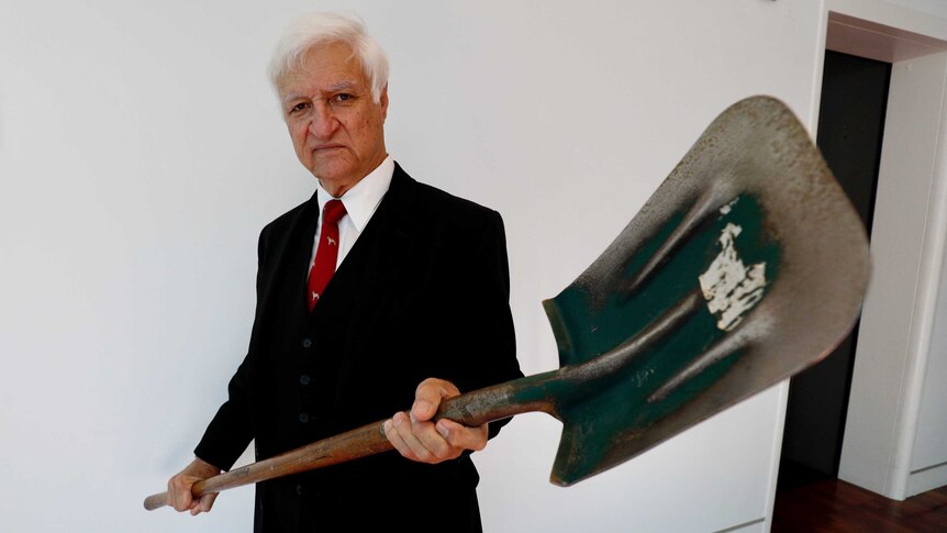 Bob Katter holds a shovel with the digging end near the camera lens
