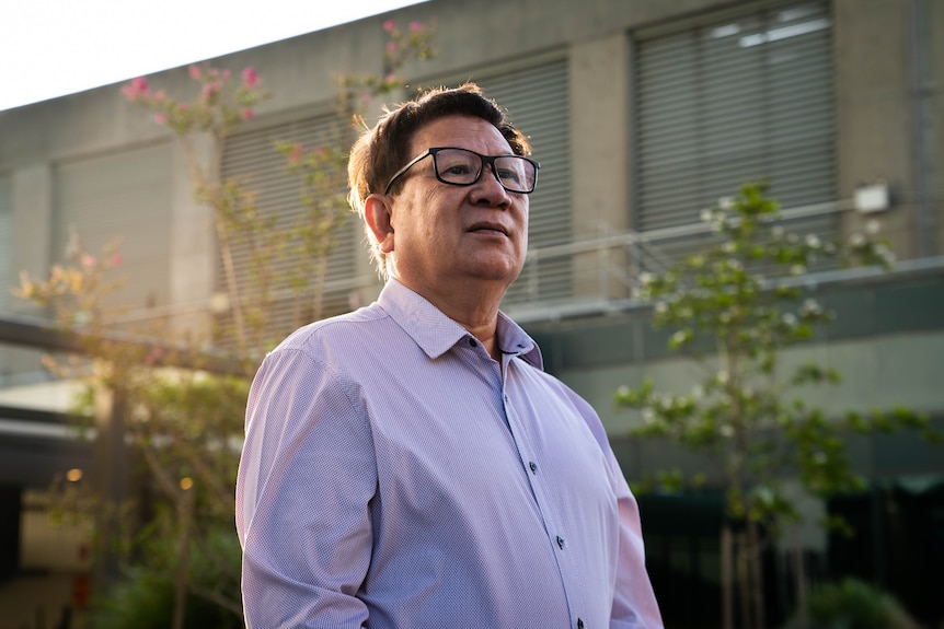 an asian man in glasses and a collared shirt with the sunset on his back