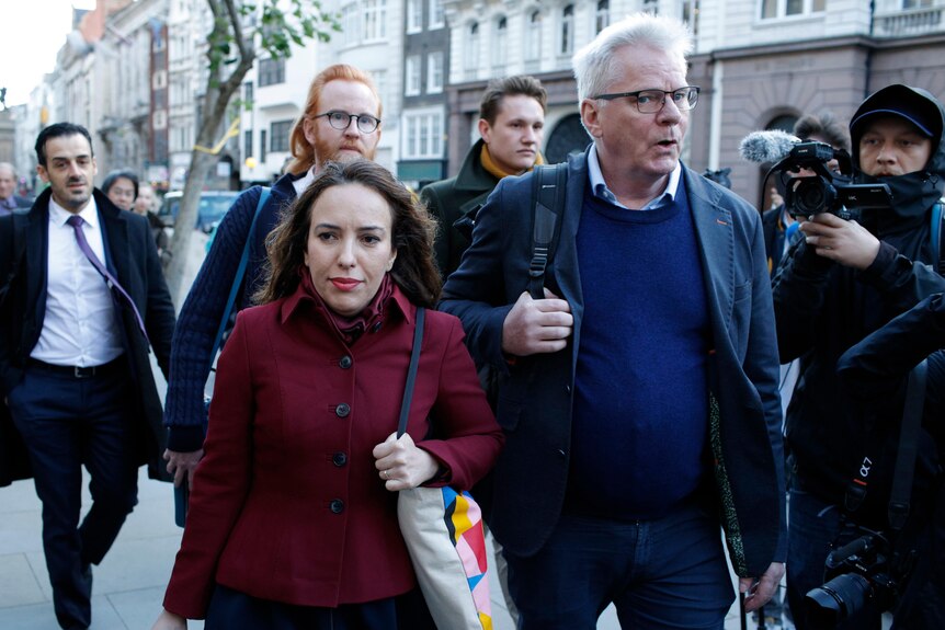 A woman in a red coat walks next to a man in a blue suit jacket