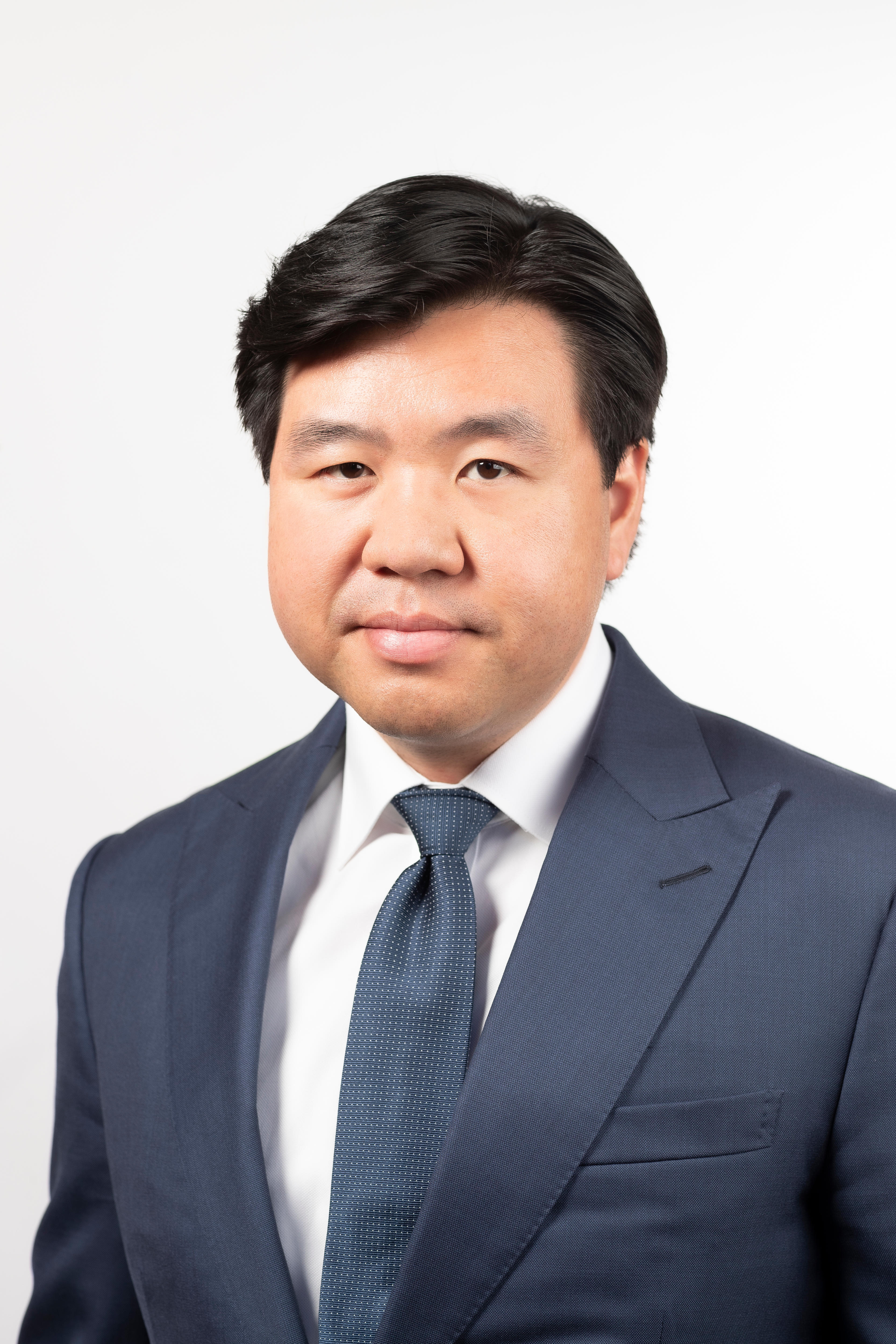 Middle aged man with dark hair in a suit smiles at camera