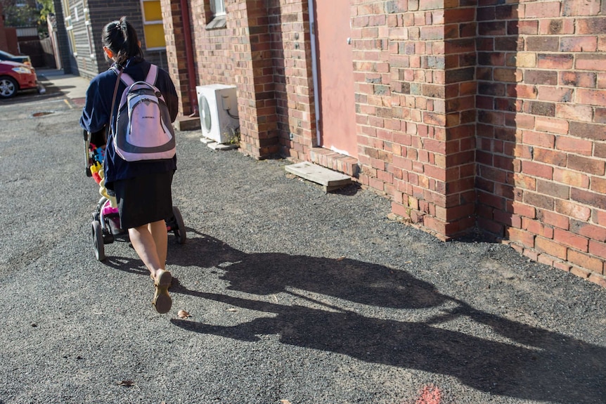 Layla, wearing a pink backpack, pushes her daughter down the street in a stroller.