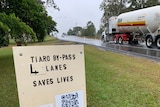 A sign saying "4 lanes saves lives" on a busy road.