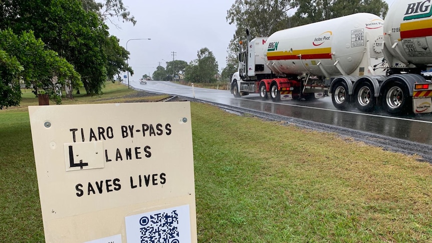 A sign saying "4 lanes saves lives" on a busy road.