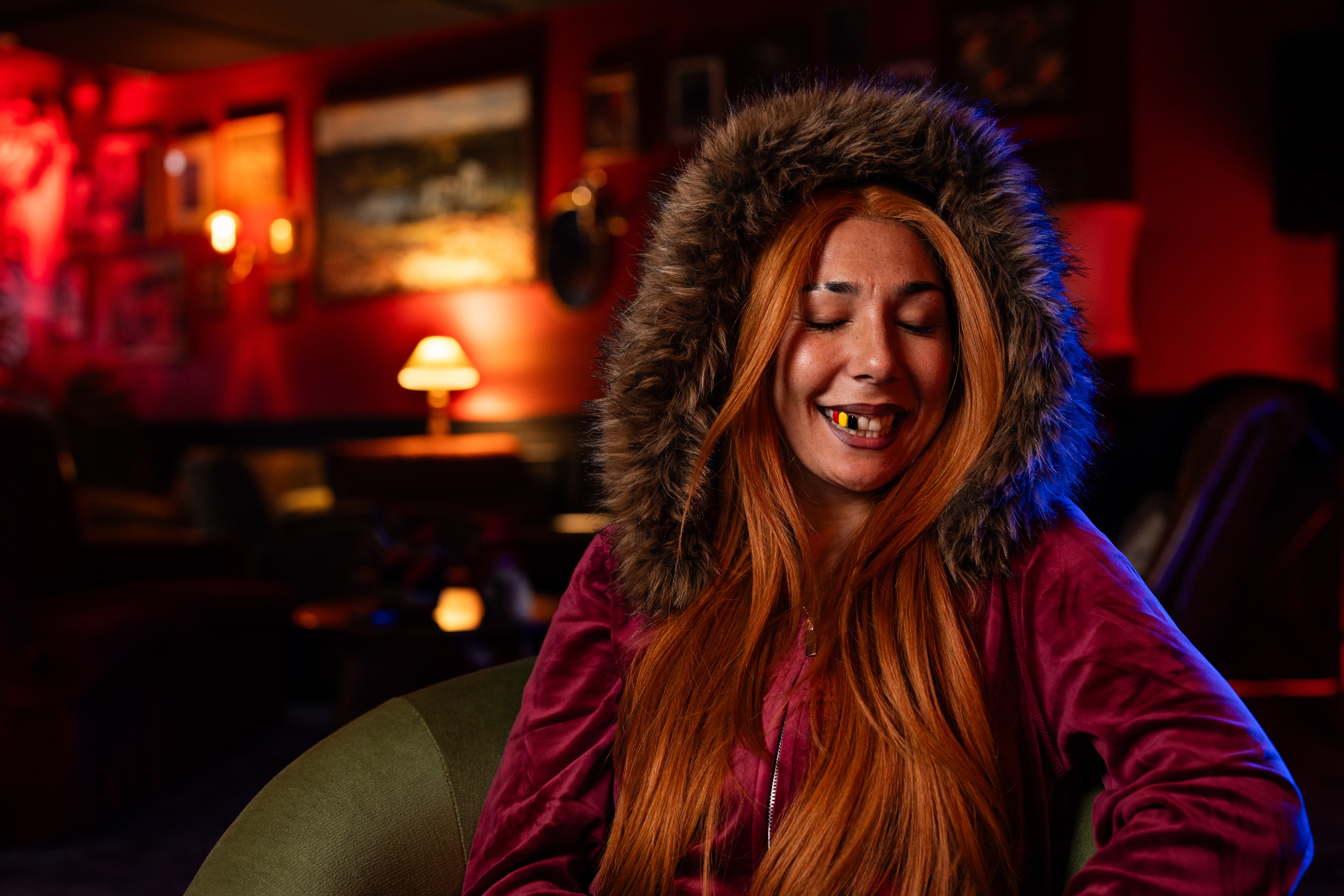 Miss Kaninna sits in an armchair in a room with red lighting and sings.