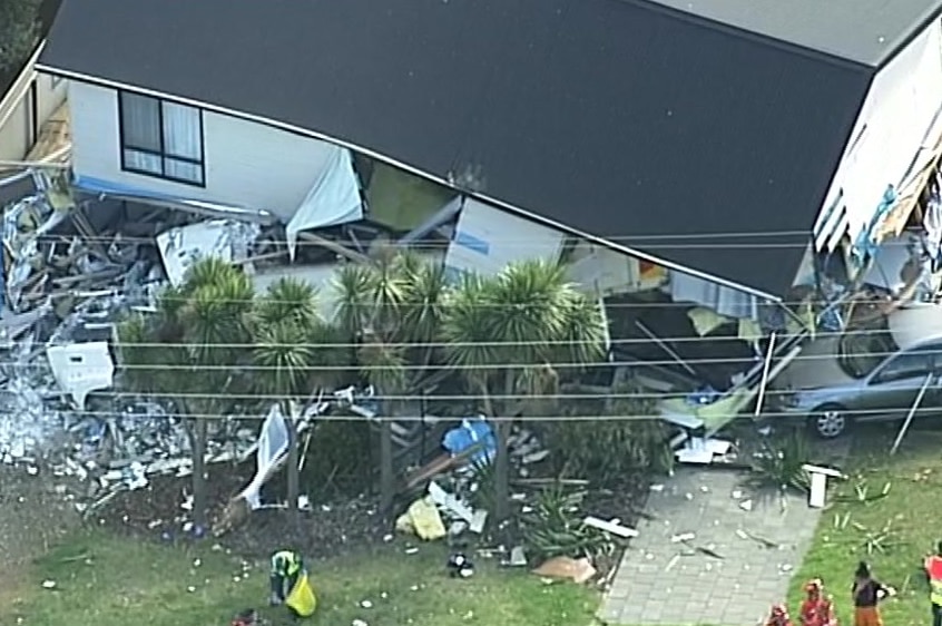 A two-storey white house with a grey roof destroyed by the impact of a truck crash.